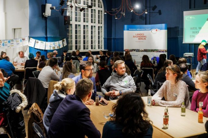 Politischer Abend des LJR Gruppen von Menschen diskutieren in einem hell erleuchteten Raum bei einer Veranstaltung des Landesjugendring Berlin.