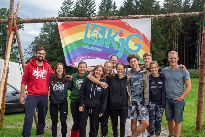 10 Jahre im Zeltlagerteam Gruppe von Jugendlichen vor einem bunten, regenbogenfarbenen Banner der KjG.